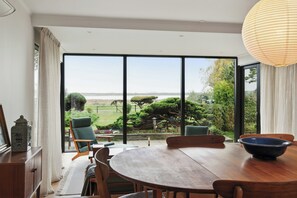 Ein Essbereich mit einem großen Tisch, Stühlen und Blick auf Garten und Gewässer.