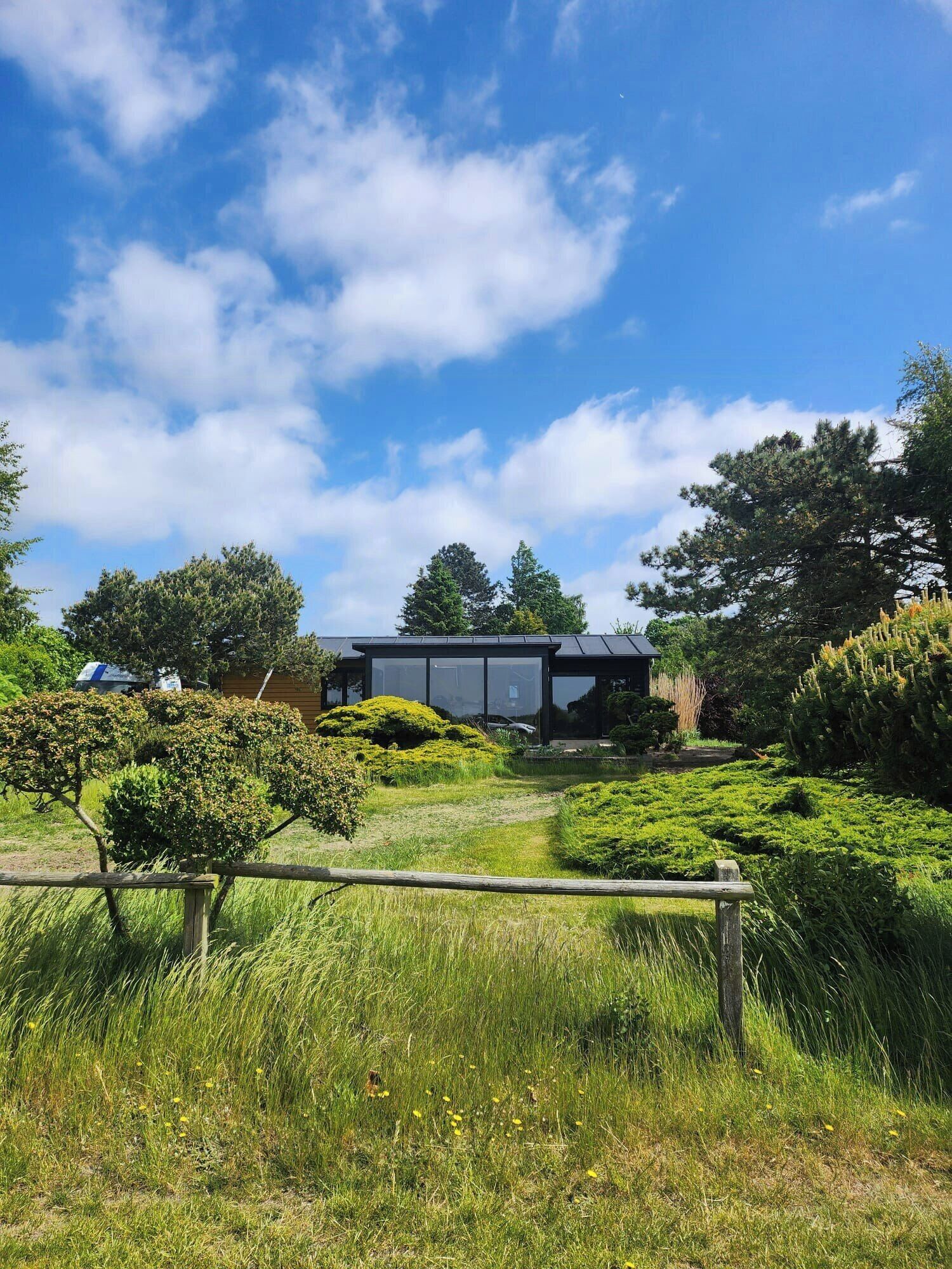 Ein modernes Haus mit Glasfassade, umgeben von üppigem Grün und blauem Himmel.