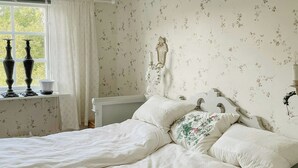 Un dormitorio con cama doble, mesita de noche, lámpara de pared y ventana con cortinas.