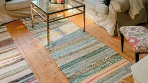 Una sala de estar con sofá, una mesa de centro de vidrio, un tapete a rayas y una ventana con cortinas.