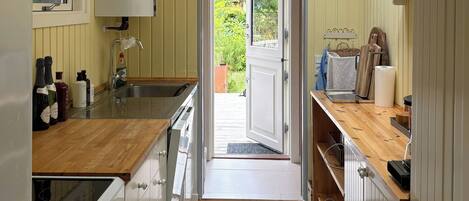 A narrow kitchen with a wooden countertop, a window, and a door leading outside.