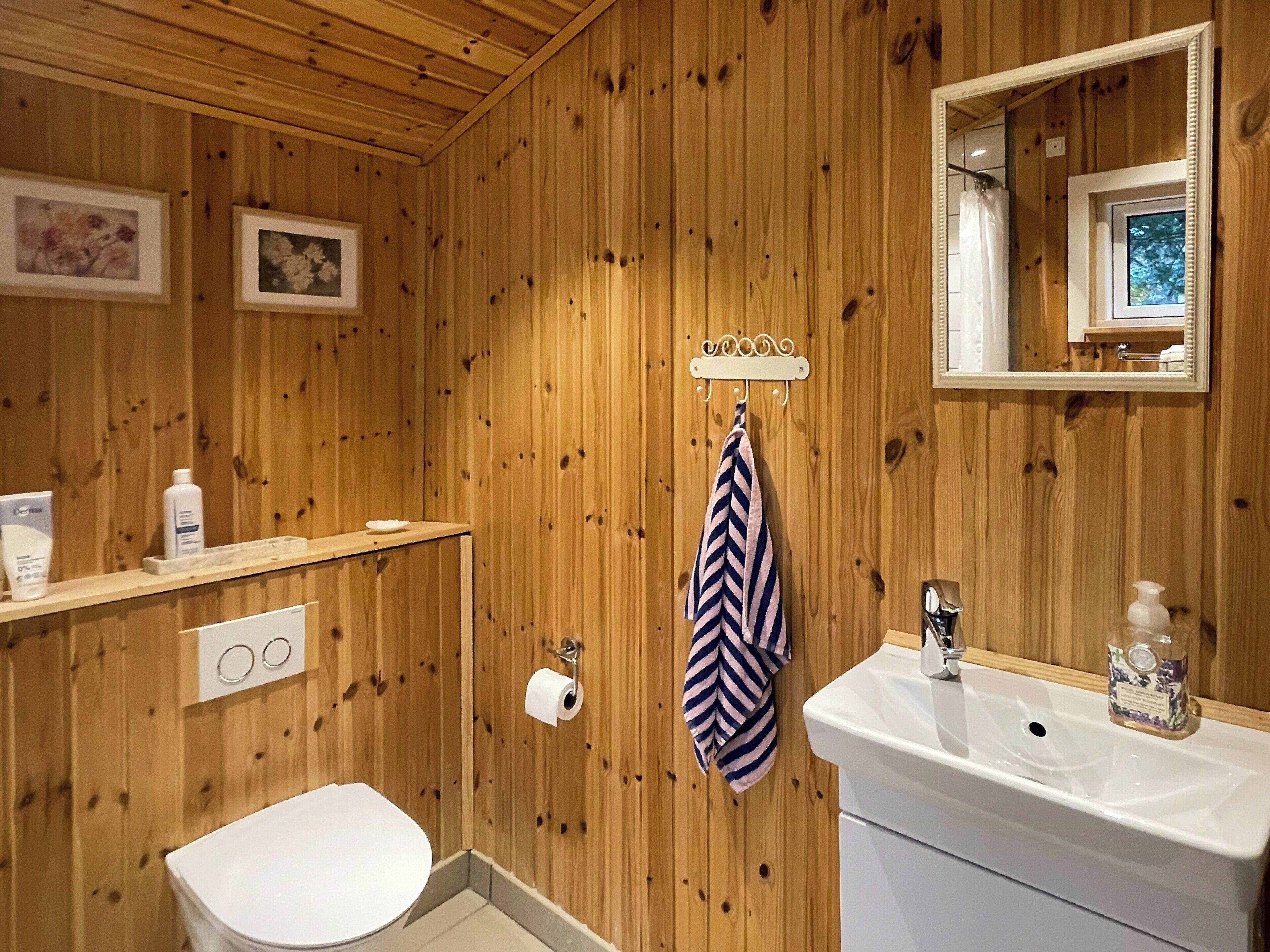A wooden-paneled bathroom with a toilet, sink, towel rack, and framed pictures on the wall.