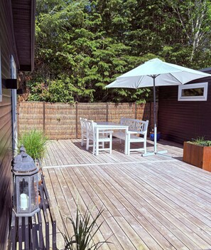 Eine Holzterrasse mit Tisch, Stühlen, einer Laterne und einem großen Sonnenschirm.