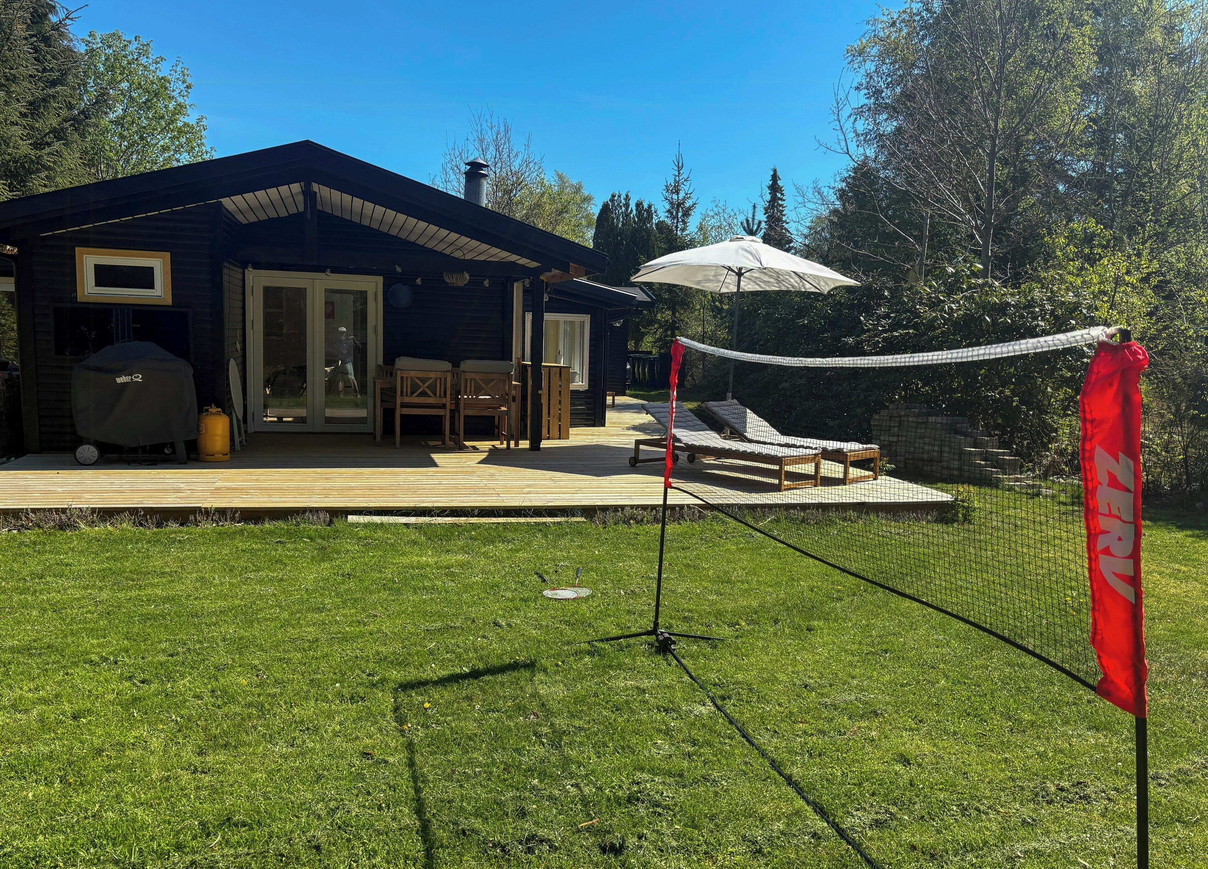 Una casa con terraza, mobiliario exterior y una red de voleibol.