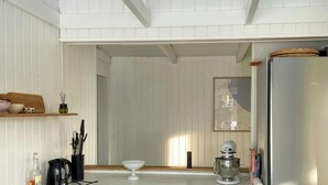 A modern kitchen with white cabinetry, a stainless steel refrigerator, and a hanging pendant light. - Architect-designed cottage by the water (Middelfart)