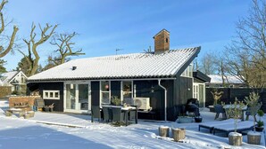 A house with a snow-covered roof, a brick chimney, and a covered patio area with outdoor furniture. - Architect-designed cottage by the water (Middelfart)