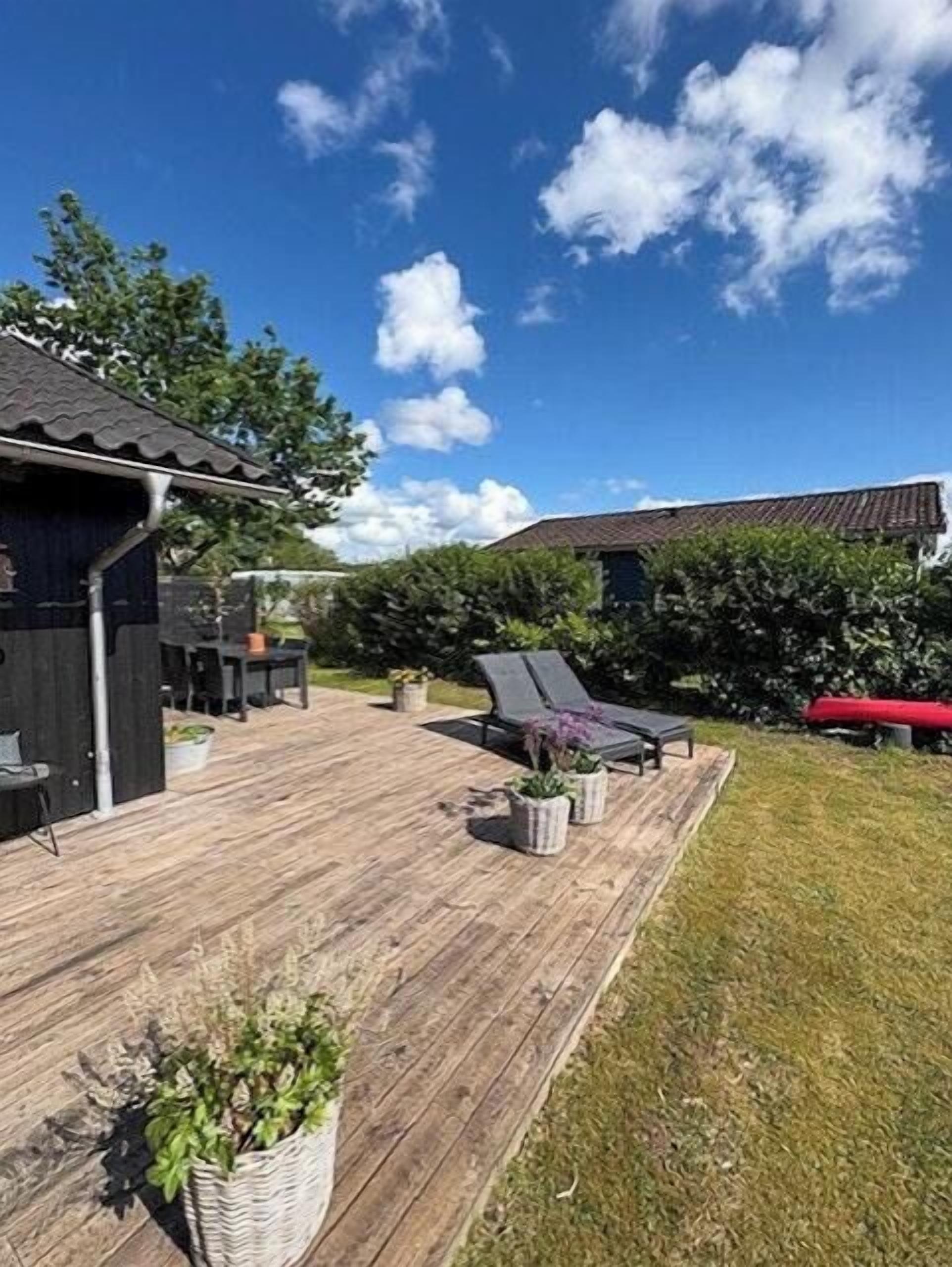 A wooden deck with outdoor furniture, a red car, and a building with a dark exterior.