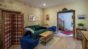 Ein Wohnzimmer mit einem grünen Sofa, blauen Sesseln, einem Holztisch und einer karierten Tür, sowie einer Treppe, die in einen anderen Raum führt.