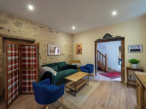Ein Wohnzimmer mit einem grünen Sofa, blauen Sesseln, einem Holztisch und einer karierten Tür, sowie einer Treppe, die in einen anderen Raum führt.