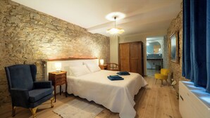 Ein Schlafzimmer mit Steinsandsteinwand, einem Bett, einem Sessel, einem Nachttisch und einem Fenster mit Vorhängen.