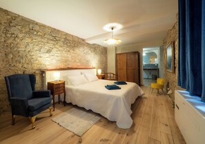 Ein Schlafzimmer mit Steinsandsteinwand, einem Bett, einem Sessel, einem Nachttisch und einem Fenster mit Vorhängen.