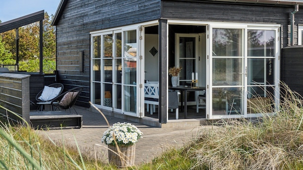 Ett modernt hus med en täckt uteplats, stora fönster och en matplats som syns genom glasdörrarna.
