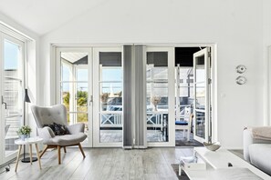 Ein modernes Wohnzimmer mit einem grauen Sessel, einem weißen Sofa, einem kleinen Tisch mit einer Pflanze und einer großen Glasschiebetür, die zu einem Außenbereich führt.