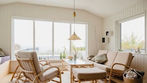 Een kamer met een groot raam, een eettafel, rieten meubels en een hanglamp.