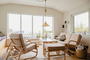 Ein Zimmer mit großem Fenster, einem Esstisch, Korbmöbeln und einer Pendelleuchte.