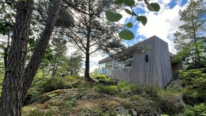 Eine moderne Holzblockhütte, umgeben von dichtem Wald, mit blauem Himmel darüber.
