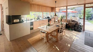 Eine moderne Küche mit Holzausstattung, ein Essbereich mit Tisch und Stühlen sowie ein großes Fenster mit Blick auf einen Garten.