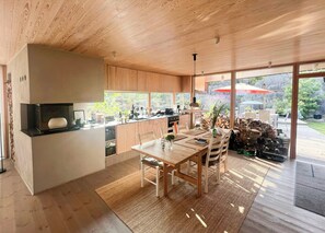 Eine moderne Küche mit Holzausstattung, ein Essbereich mit Tisch und Stühlen sowie ein großes Fenster mit Blick auf einen Garten.