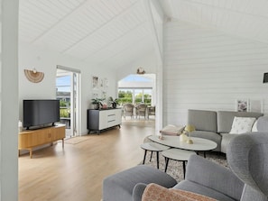 A spacious living area with a flat-screen TV, a grey sofa, and a dining table.