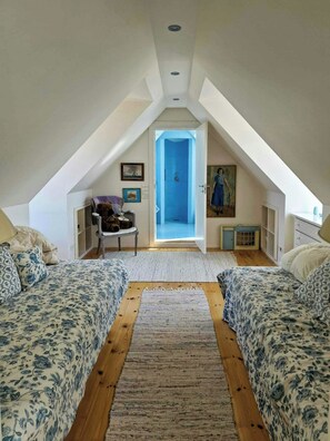 Ein Schlafzimmer mit schrägen Wänden, einem Bett mit floralem Bettzeug, einem kleinen Schreibtisch und einem Bild an der Wand.