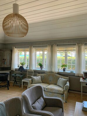 Ein Zimmer mit einer Couch, Stühlen, einem Tisch, einer Hängelampe und Fenstern mit Vorhängen.