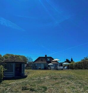 Ein Haus mit großem Rasen, einem kleinen Gartenhaus und einem Gazebo mit Sitzgelegenheiten.