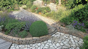Een tuin met een pad van stenen, een bakstenen rand en diverse planten.