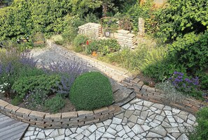 Ein Garten mit einem gepflasterten Weg, einer Ziegelumrandung und verschiedenen Pflanzen.