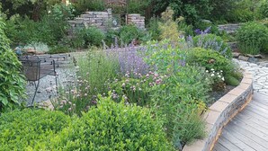 Een tuin met stenen muren, verschillende planten en een houten terras.