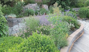 Ein Garten mit Steinmauern, unterschiedlichen Pflanzen und einer Holzterrasse.