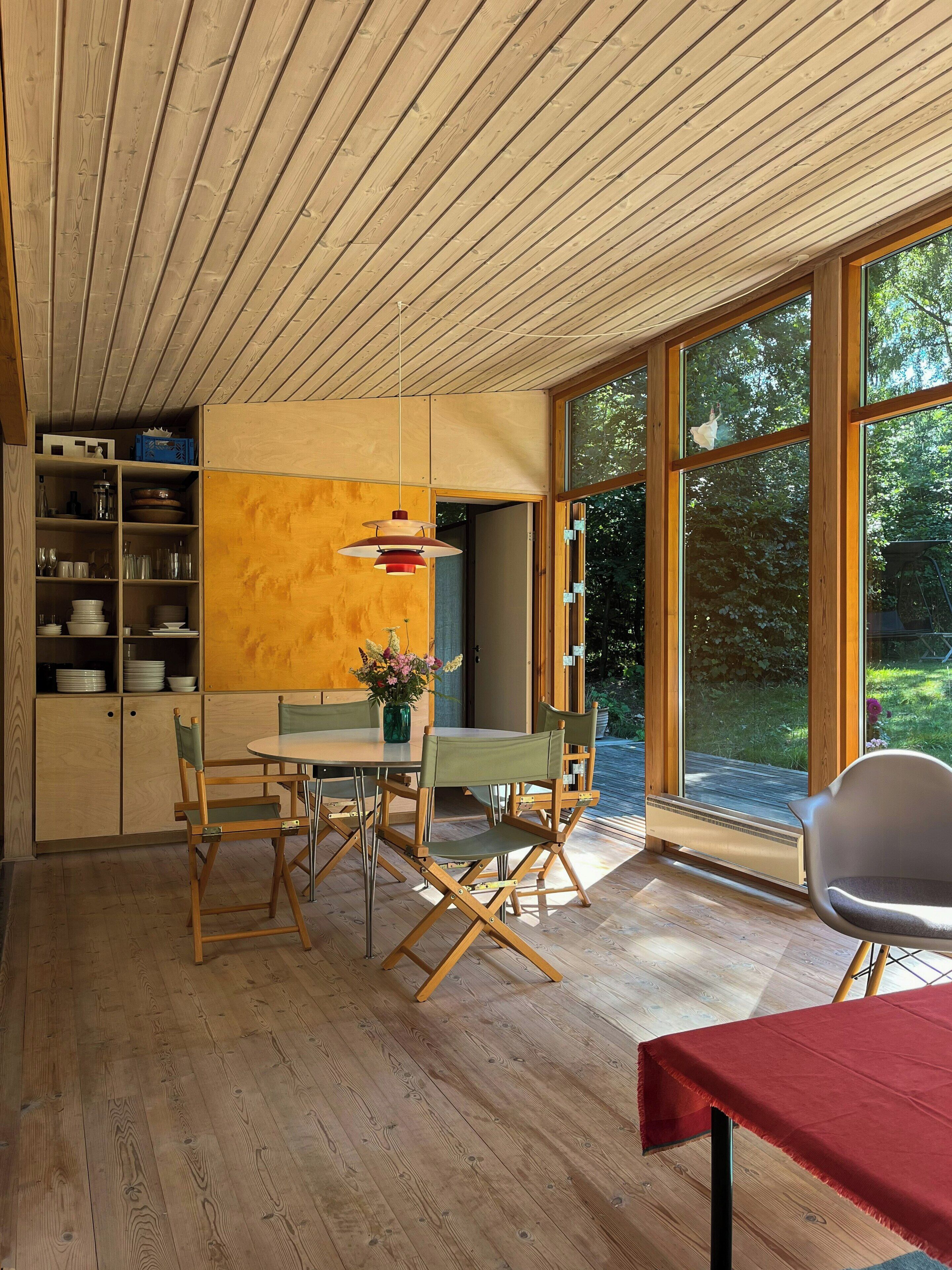 A dining area with a wooden table, chairs, and a view of greenery outside.