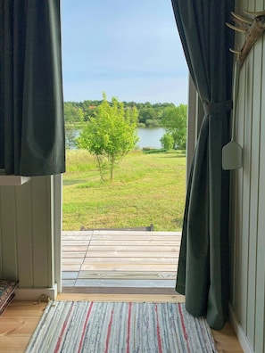 Huone, josta on näkymä järvelle, ja jossa on puinen terassi sekä raidallinen matto.