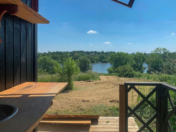 A wooden deck with a view of a lake and surrounding greenery. - Shepherd's hut with lake view in Ollerup (Vester Skerninge)