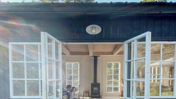 Une cabane en bois dotée de grandes fenêtres, d’une cheminée et d’une terrasse.