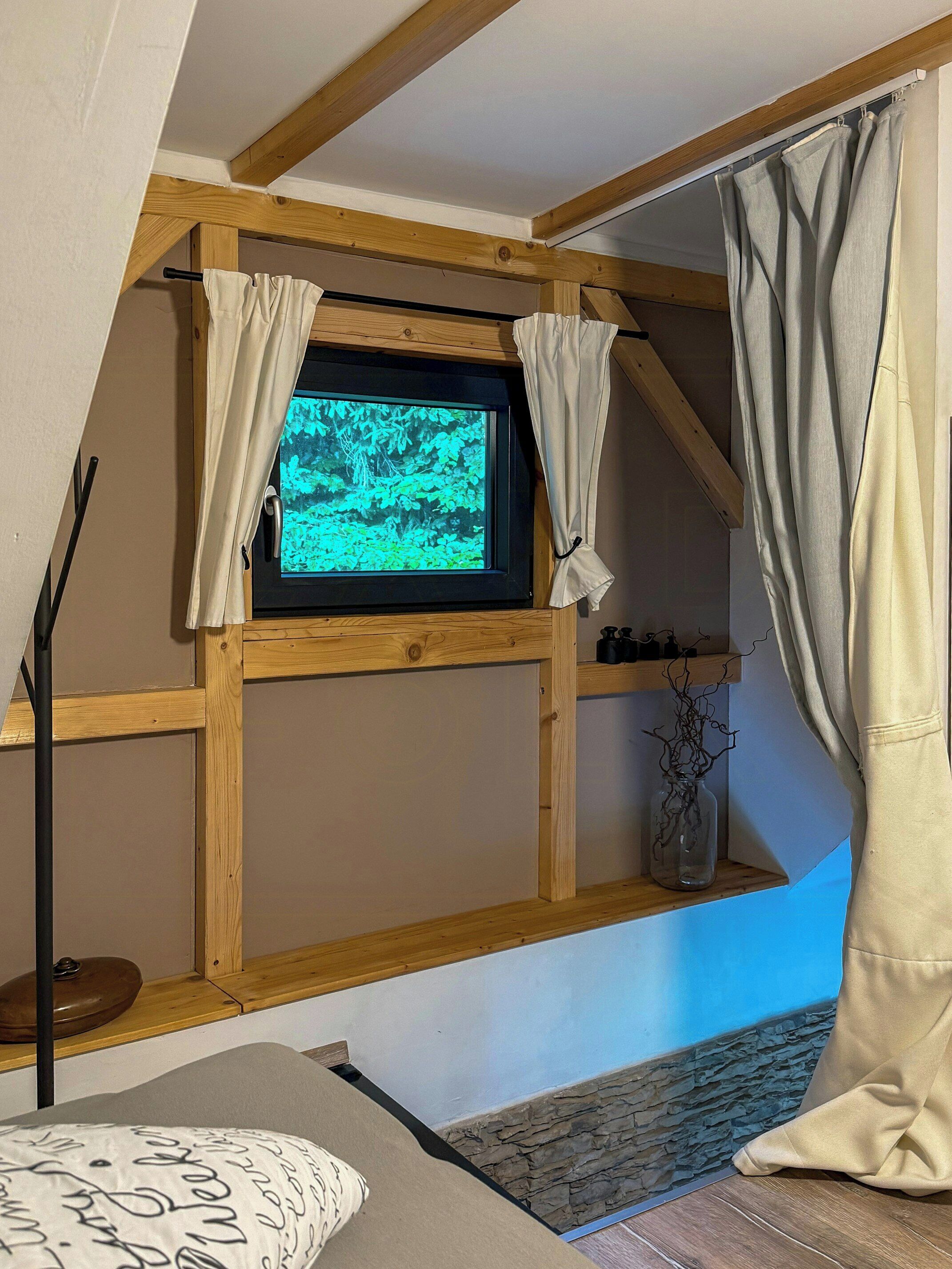 Ein Zimmer mit Holzboden, einem an der Wand montierten Fernseher, einem Bett mit einem gemusterten Kopfkissen und einer Steinwand.