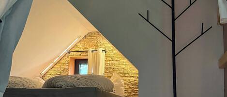 A bedroom with a sloped ceiling, a bed, a coat rack, and a small window.