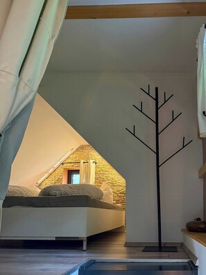 Un dormitorio con techo inclinado, una cama, un perchero y un ventanal pequeño.