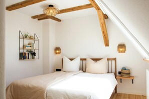 Ein Schlafzimmer mit einem Bett, Holzbalken, einem an der Wand montierten Bücherregal und zwei Wandleuchten.