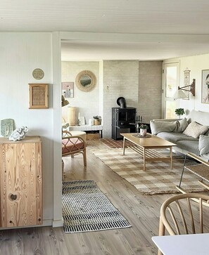 A cozy living room with a fireplace, a sofa, a coffee table, and a wooden cabinet. - House among dunes and trees in Søndervig (Ringkøbing)