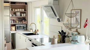 A modern kitchen with white cabinetry, a central island, a microwave, and a hanging light fixture. - House among dunes and trees in Søndervig (Ringkøbing)