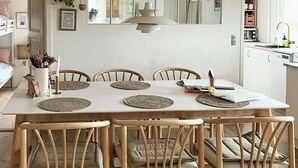 A dining area with a white table, wooden chairs, woven placemats, and a hanging pendant light. - House among dunes and trees in Søndervig (Ringkøbing)