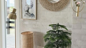 A room with a concrete wall, a round woven mirror, a framed picture, a potted plant, a candle, and a hanging gold ring. - House among dunes and trees in Søndervig (Ringkøbing)