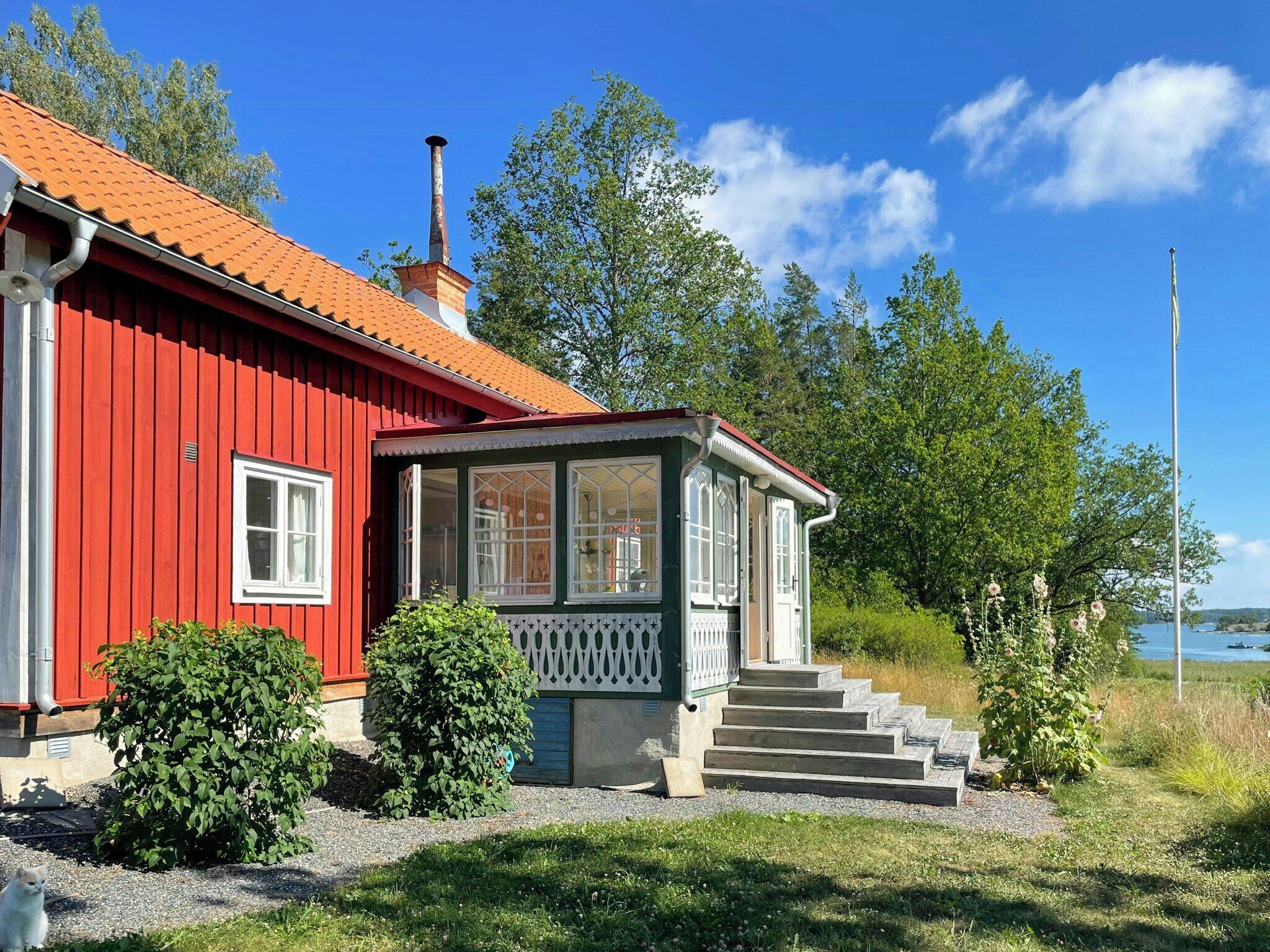 A red wooden house with a chimney, a porch with steps, and a view of the water.