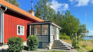 A red wooden house with a chimney, a porch with steps, and a view of the water.