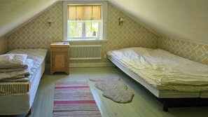 Ein kleines Schlafzimmer im Dachgeschoss mit zwei Einzelbetten, einem Holznachttisch, einem Heizkörper und einem Fenster mit Vorhängen.