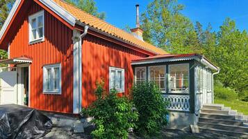A red wooden house with a chimney, a porch with white trim, and a small garden.