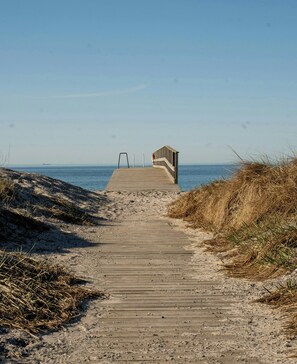 Ein hölzerner Steg führt zu einem Strand, am Ende befindet sich ein Holzbau.