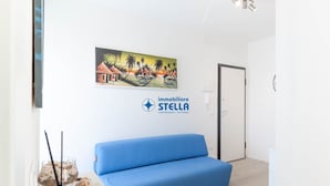 Quarto com sofá azul, um quadro na parede e o logotipo da 'immobiliare STELLA'.