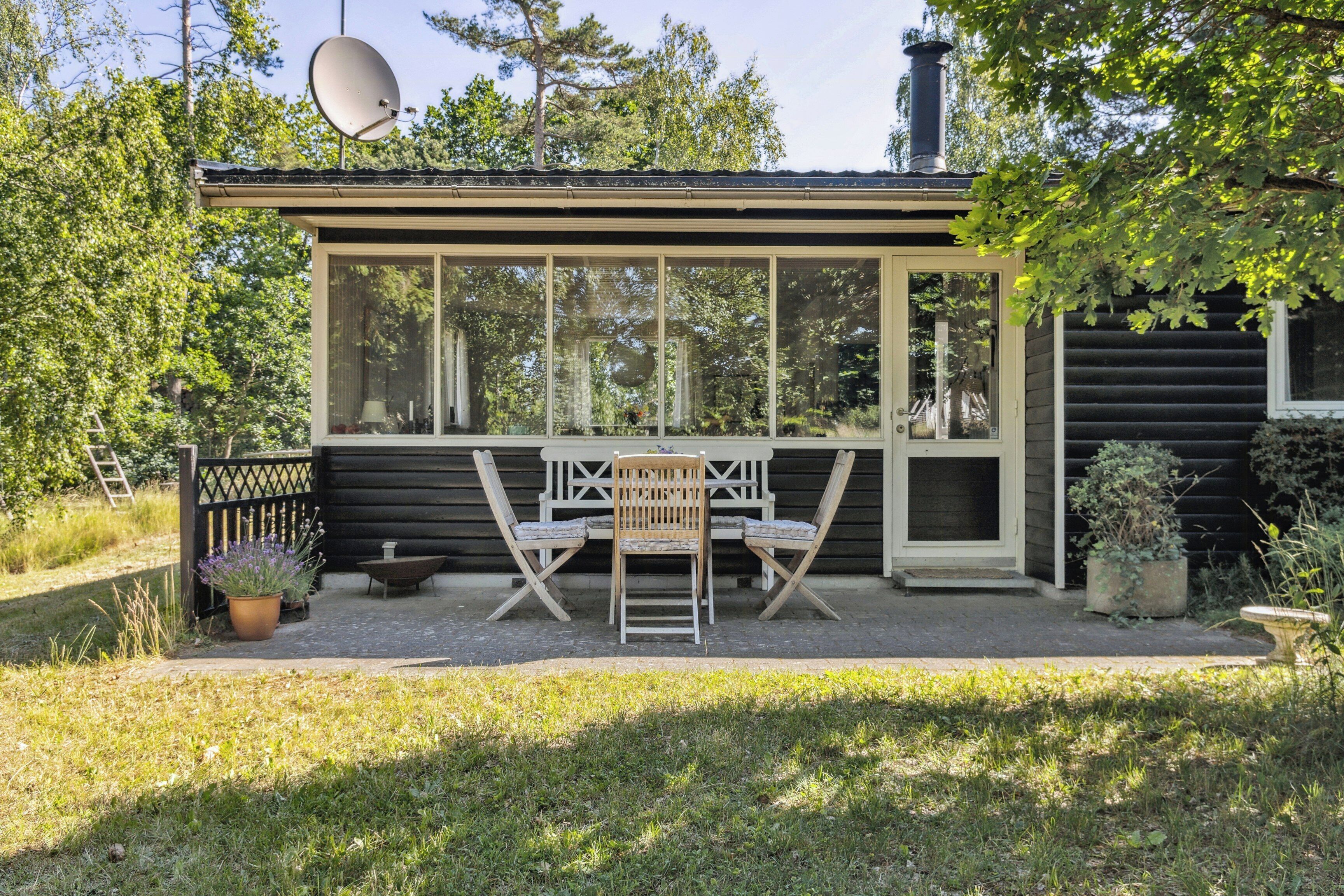 A small wooden cabin with a large window, a satellite dish, and a patio with a table and chairs.
