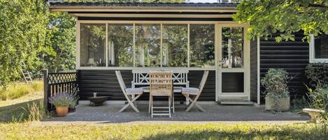 A small wooden cabin with a large window, a satellite dish, and a patio with a table and chairs.
